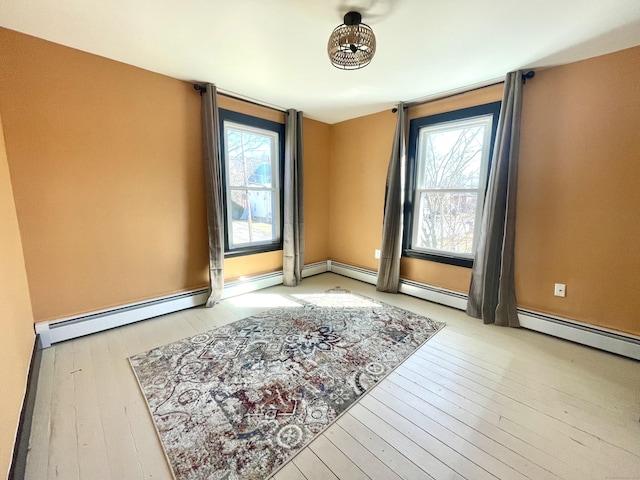 spare room with a baseboard heating unit, hardwood / wood-style flooring, and baseboards