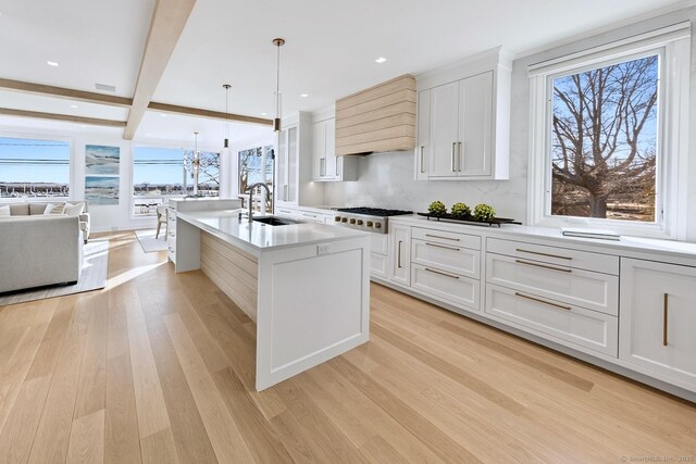 kitchen with beam ceiling, light wood finished floors, custom range hood, white gas cooktop, and a sink