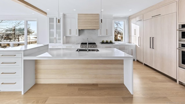 kitchen with a center island with sink, custom range hood, light countertops, light wood-style floors, and a sink