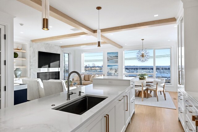 kitchen featuring beamed ceiling, a sink, light wood-style flooring, and white cabinets