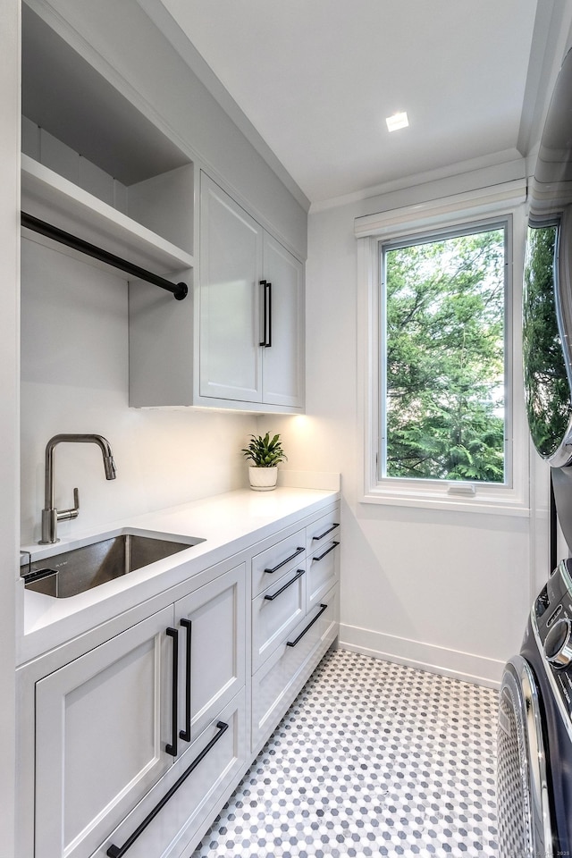 kitchen featuring baseboards, white cabinets, stacked washer / drying machine, light countertops, and a sink