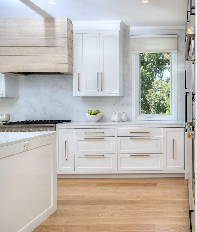 kitchen featuring light wood finished floors, tasteful backsplash, white cabinets, light countertops, and wall chimney range hood