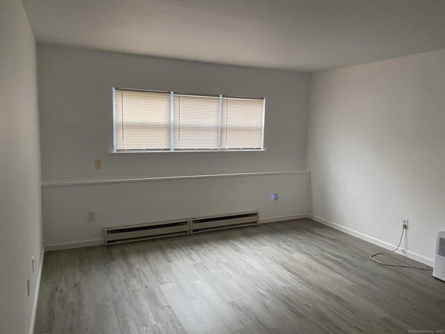 unfurnished room with a baseboard radiator, wood finished floors, and baseboards