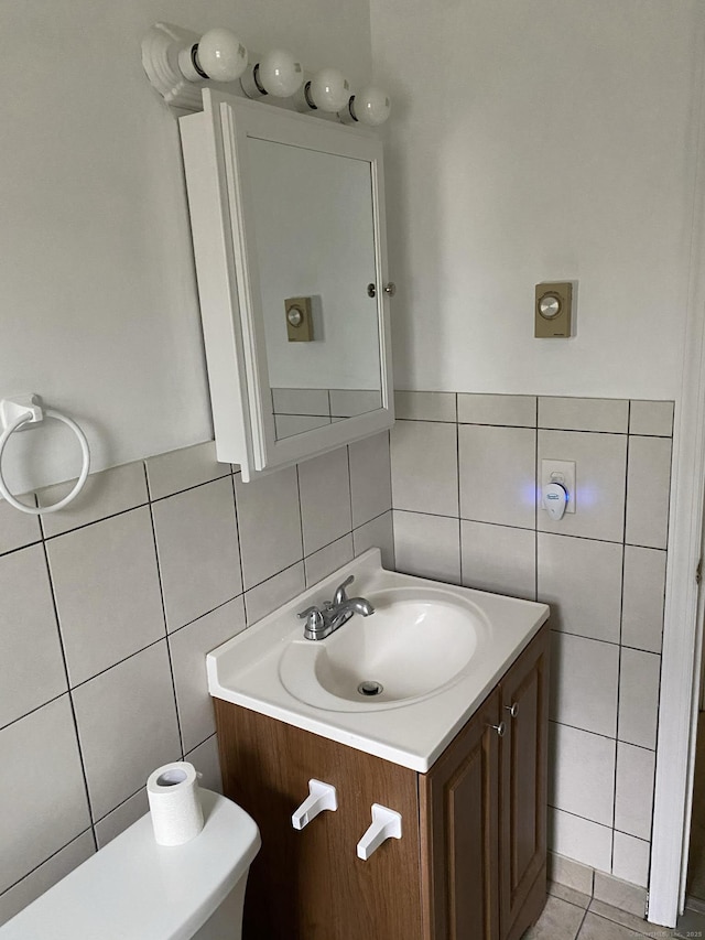 half bath with tile patterned flooring, vanity, and tile walls