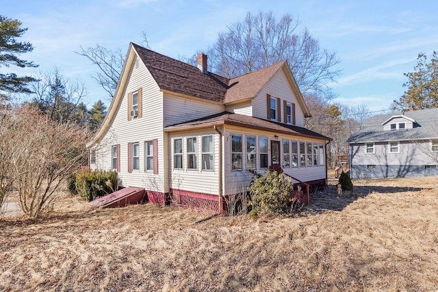 view of side of property with a sunroom, a shingled roof, and a chimney