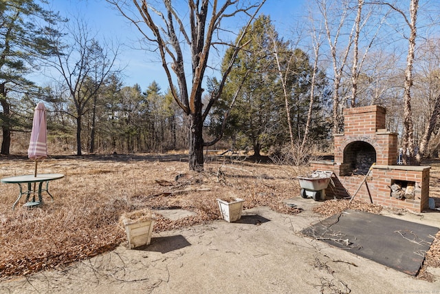 view of yard featuring an outdoor brick fireplace and a patio area