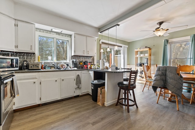 kitchen featuring stainless steel appliances, dark countertops, white cabinets, a sink, and a peninsula