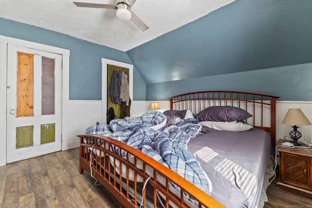 bedroom featuring a wainscoted wall, ceiling fan, wood finished floors, vaulted ceiling, and a closet