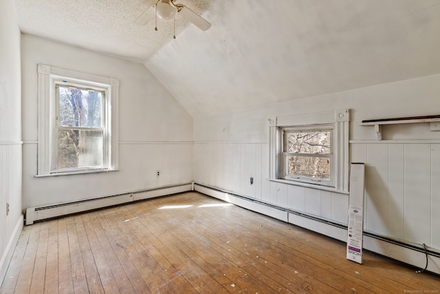 additional living space featuring lofted ceiling, wood-type flooring, a baseboard radiator, a ceiling fan, and a textured ceiling