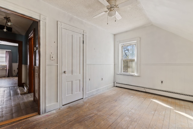 additional living space featuring hardwood / wood-style flooring, a baseboard radiator, a textured ceiling, and wainscoting