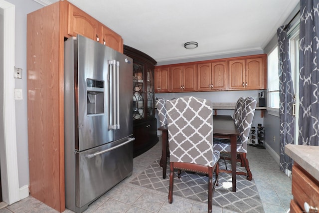 kitchen featuring light countertops, light tile patterned flooring, brown cabinetry, and stainless steel fridge