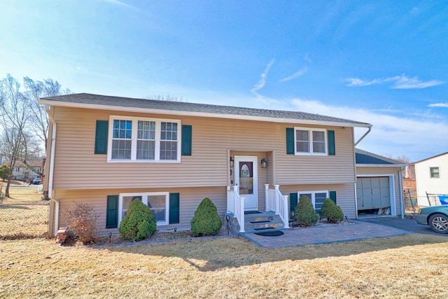 raised ranch featuring an attached garage, a front yard, and fence