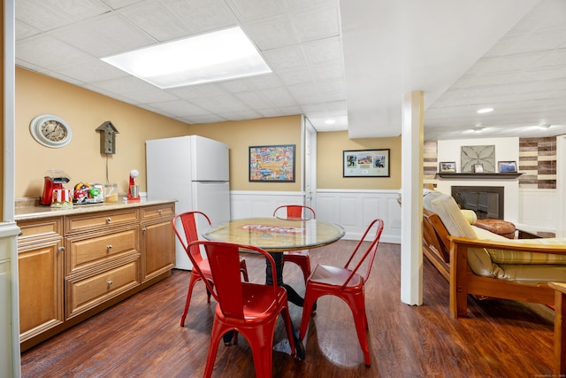 dining space featuring dark wood-type flooring, a paneled ceiling, a fireplace, and wainscoting