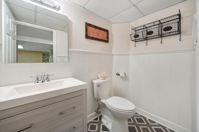 bathroom featuring a paneled ceiling, toilet, wainscoting, and vanity