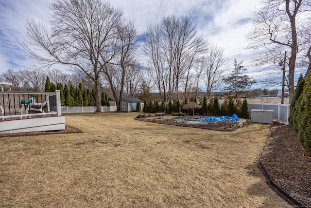 view of yard featuring an outbuilding, a shed, a wooden deck, a fenced backyard, and a swimming pool