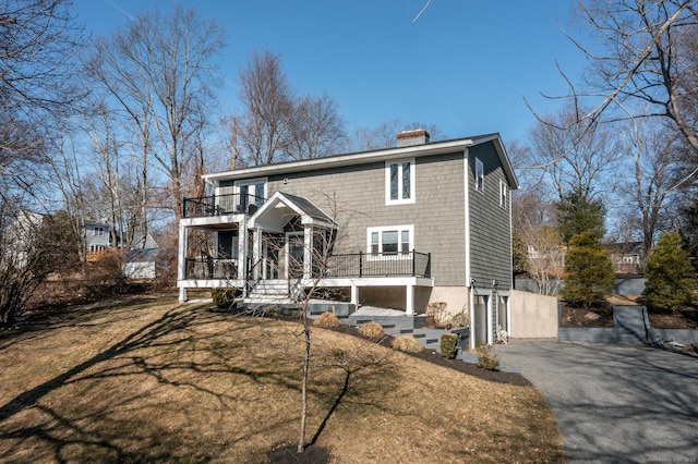 view of front of property featuring a front lawn, driveway, an attached garage, a balcony, and a chimney