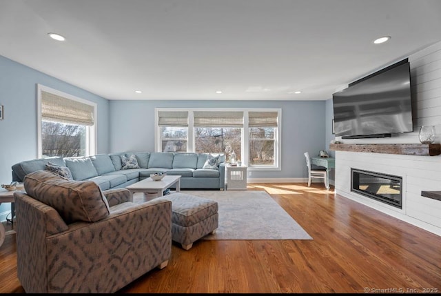 living area with a glass covered fireplace, baseboards, recessed lighting, and wood finished floors