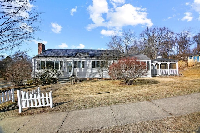 view of front facade featuring a fenced front yard, roof mounted solar panels, a chimney, and a gazebo