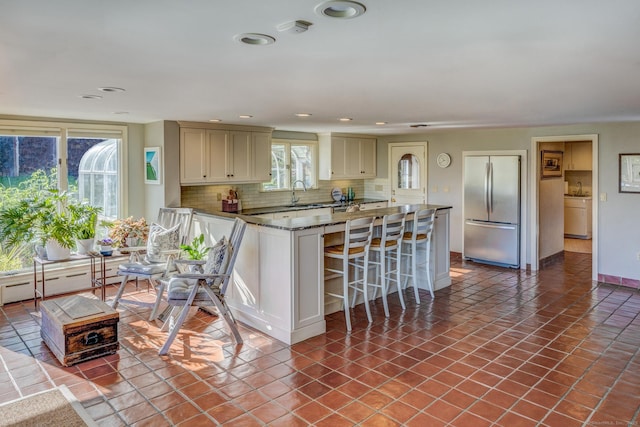 kitchen featuring tasteful backsplash, tile patterned floors, freestanding refrigerator, a kitchen bar, and a sink