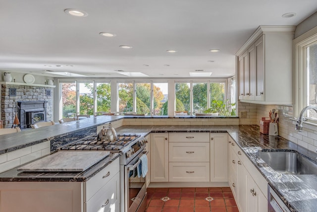 kitchen with stainless steel appliances, a fireplace, a sink, tile patterned floors, and tasteful backsplash