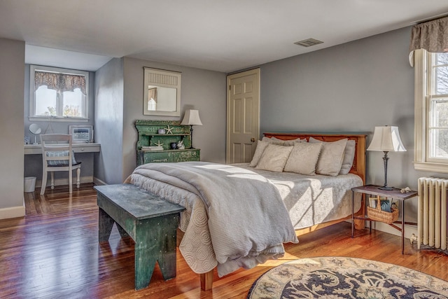 bedroom with radiator, visible vents, baseboards, and wood finished floors