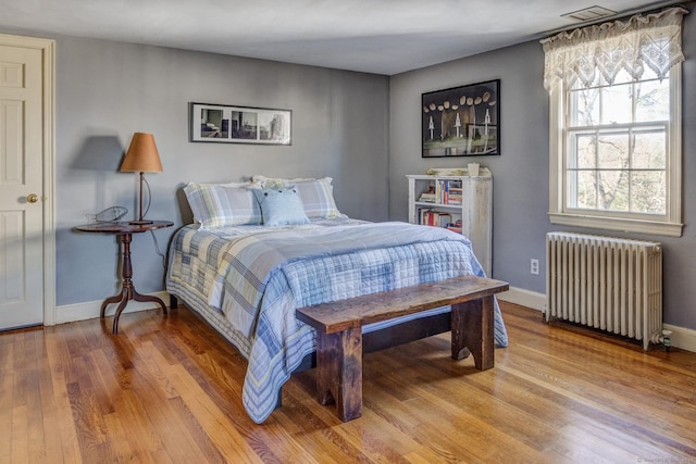 bedroom featuring radiator, baseboards, visible vents, and wood finished floors