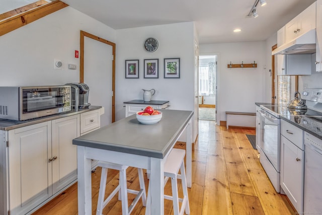 kitchen with white appliances, light wood-style floors, dark countertops, under cabinet range hood, and white cabinetry