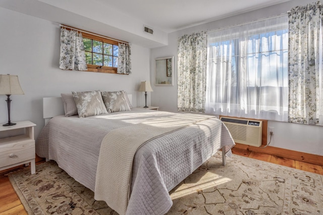 bedroom featuring a wall unit AC, wood finished floors, and visible vents