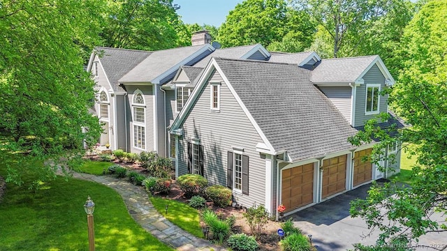 view of home's exterior with driveway, a shingled roof, a chimney, an attached garage, and a yard