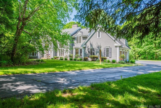 view of front of home featuring a garage, driveway, a chimney, and a front lawn