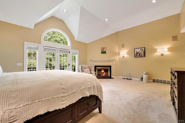 bedroom with access to exterior, light colored carpet, visible vents, a fireplace with flush hearth, and high vaulted ceiling