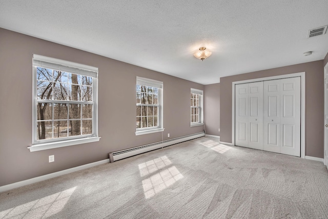 unfurnished bedroom featuring a textured ceiling, visible vents, baseboard heating, a closet, and carpet