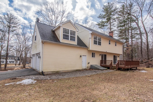 rear view of house with aphalt driveway, a chimney, a shingled roof, a deck, and a garage