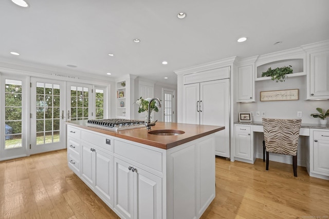 kitchen with open shelves, stainless steel gas cooktop, light wood-style floors, and a sink