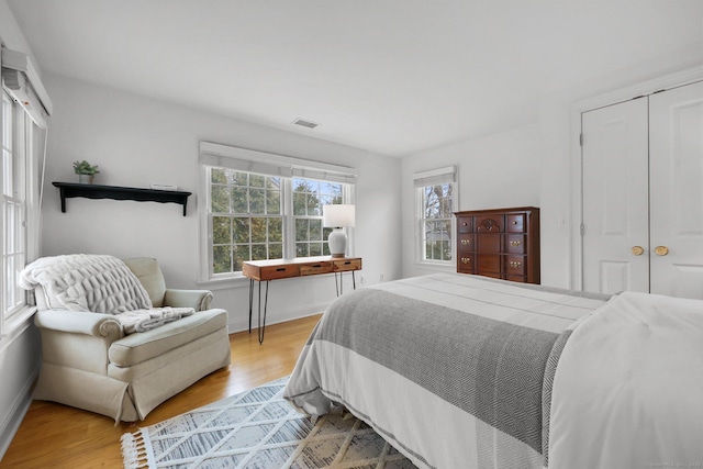 bedroom with a closet, visible vents, baseboards, and wood finished floors