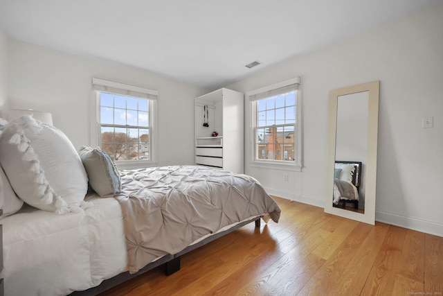 bedroom with visible vents, multiple windows, baseboards, and light wood finished floors