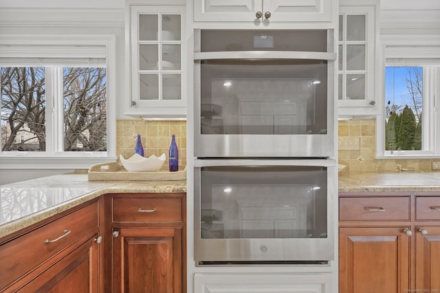 kitchen featuring tasteful backsplash, stainless steel double oven, a healthy amount of sunlight, and glass insert cabinets