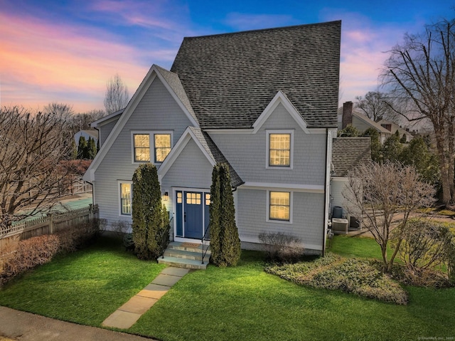 view of front of property featuring a yard, a shingled roof, and fence