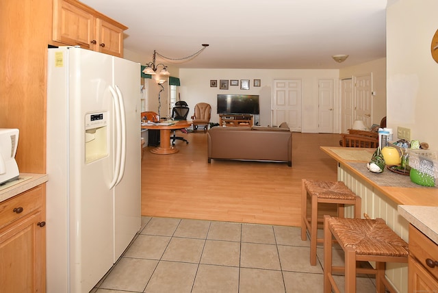 kitchen featuring light tile patterned floors, white refrigerator with ice dispenser, open floor plan, light countertops, and light brown cabinetry