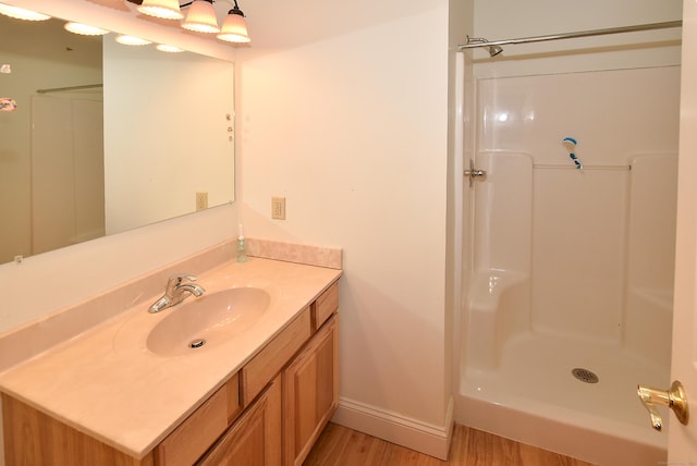 full bath featuring wood finished floors, vanity, baseboards, and walk in shower