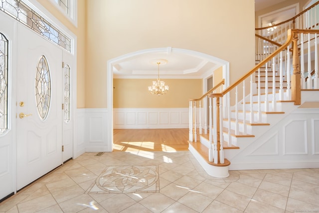 foyer featuring a chandelier, arched walkways, a decorative wall, a high ceiling, and ornamental molding