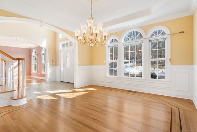 unfurnished dining area featuring arched walkways, wood finished floors, stairs, and ornamental molding