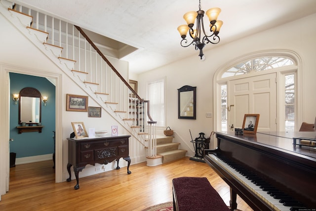 foyer entrance with light wood-style floors, stairway, baseboards, and an inviting chandelier