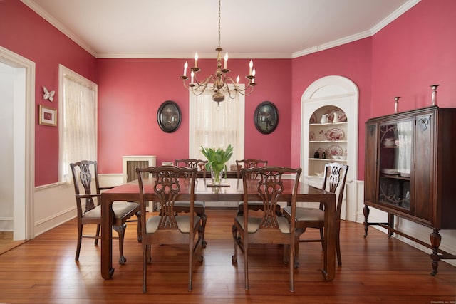 dining room with a notable chandelier, built in features, wood finished floors, and ornamental molding