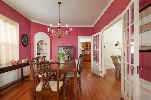 dining area featuring built in features, wood finished floors, an inviting chandelier, crown molding, and french doors