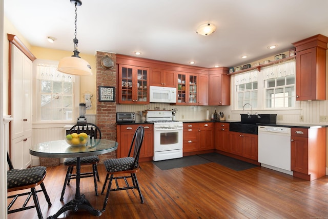 kitchen featuring white appliances, dark wood-type flooring, a sink, hanging light fixtures, and glass insert cabinets