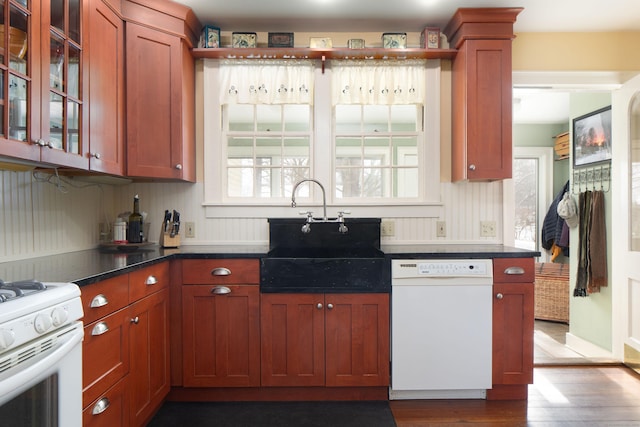 kitchen featuring dark countertops, glass insert cabinets, a sink, wood finished floors, and white appliances