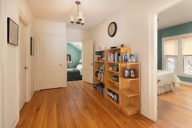 hallway with baseboards, light wood-type flooring, and an inviting chandelier