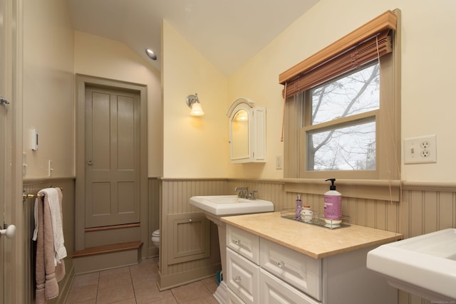 bathroom featuring lofted ceiling, toilet, wainscoting, a sink, and tile patterned flooring