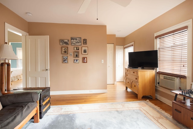 living area with light wood finished floors, cooling unit, baseboards, and a ceiling fan